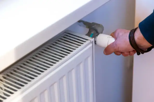 Ręka reguluje termostat grzejnika. Dowiedz się, jak wymienić kaloryfer w bloku, by cieszyć się ciepłem.