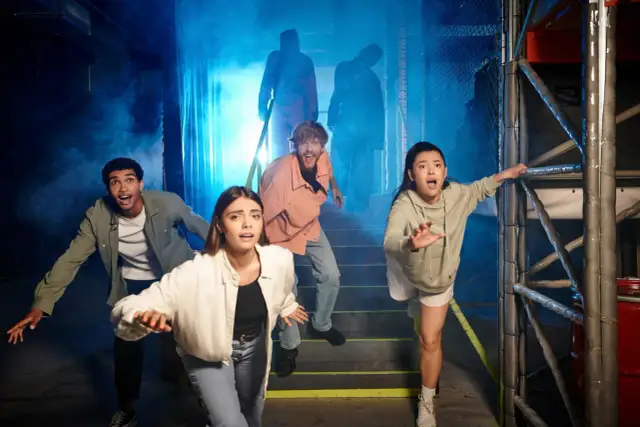 Grupa przerażonych ludzi ucieka przed postaciami w dymie. To wygląda jak prawdziwy escape room, gdzie trzeba rozwiązać zagadki, by przeżyć.