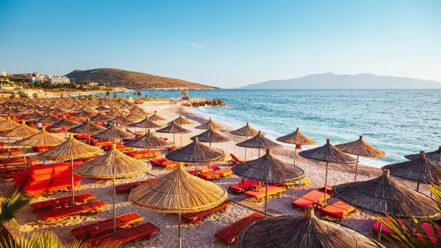 Albania, lipiec: słoneczna plaża z rzędami parasoli i leżaków, turkusowe morze i góry w tle. Idealna pogoda na wakacje.