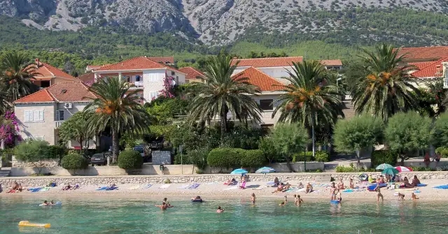 Plaża z palmami, domami i ludźmi kąpiącymi się w morzu.