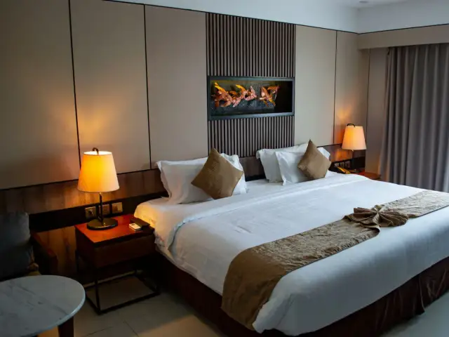 Przytulna sypialnia hotelowa z dużym łóżkiem, lampkami nocnymi i ozdobnym zagłówkiem.