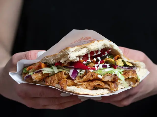 Kebab w bułce z mięsem, warzywami i sosami, trzymany w dłoniach.