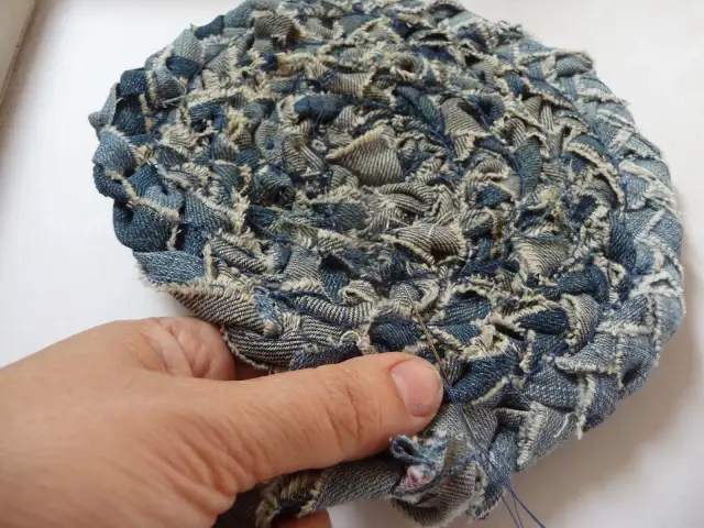 Ręka szyje okrągły dywanik z dżinsowych szmatek.