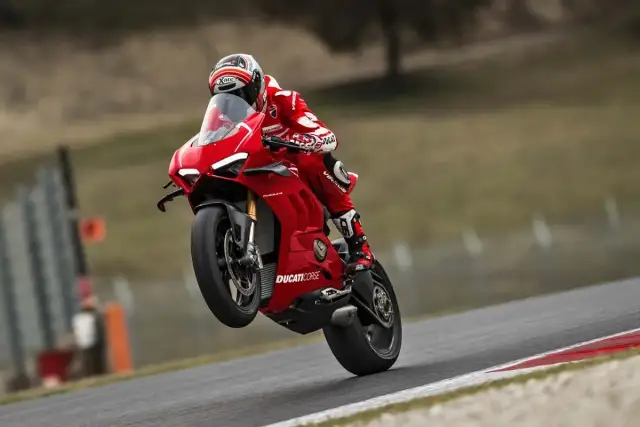 Czerwona Ducati Panigale V4R na torze, z przednim kołem w powietrzu. Kierowca w kombinezonie Ducati Corse.