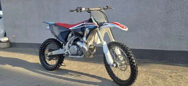 Motocykl crossowy Husqvarna CR 250 z czerwonym siedzeniem i czarnymi elementami, gotowy do jazdy po torze.