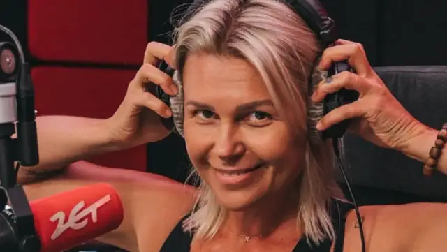 Agnieszka Kołodziejska, w wieku około 40 lat, z uśmiechem na twarzy zakłada słuchawki w studiu radiowym.