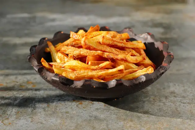 Chrupiące, złociste frytki w ciemnej misce na kamiennym tle.