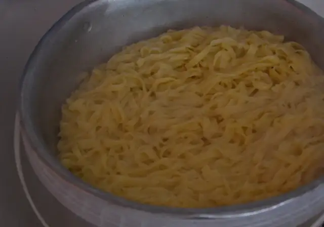 Gotowanie kluski vs makaron. Szerokie, żółte wstążki w garnku, gotowe do podania.