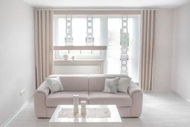 Jasny wystrój okna tarasowego z beżowymi zasłonami, sofą i stolikiem kawowym.