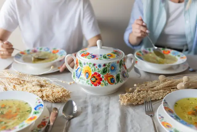Stół z miskami zupy, ozdobionymi tradycyjnymi wzorami, i ozdobnymi kłosami.