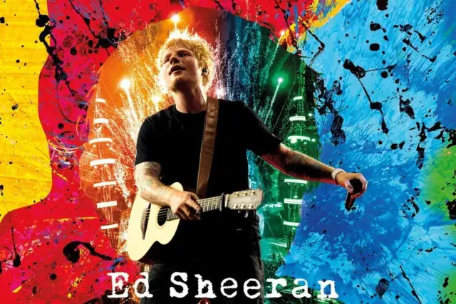 Ed Sheeran z gitarą i mikrofonem, w otoczeniu kolorowych eksplozji farby. Marzenie o koncercie kiedy Ed Sheeran zagra koncert w Polsce.