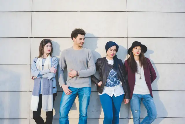 Cztery osoby w różnym stylu stojące pod ścianą.