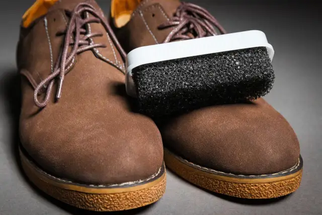 Brązowe zamszowe buty z białą szczotką do czyszczenia na jednym z nich.