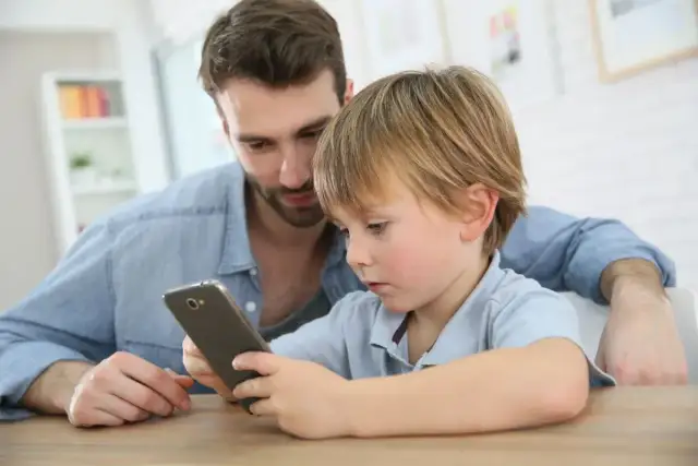 Tata pokazuje synowi jego pierwszy telefon dla dziecka. Chłopiec z zaciekawieniem ogląda ekran.