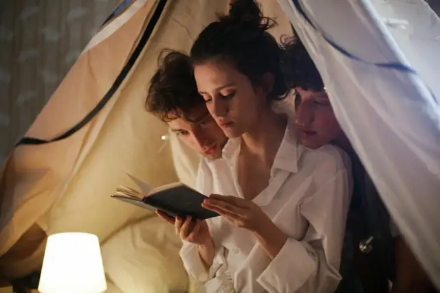 Trzy osoby czytają książkę pod kocem. Czy to przykład nie monogamii?
