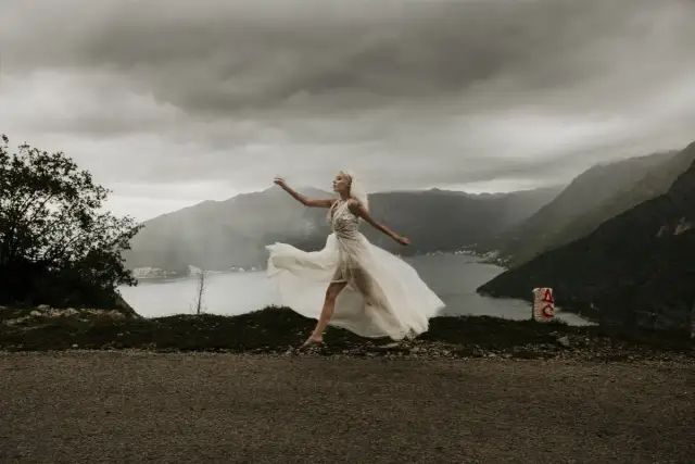 Panna młoda w zwiewnej sukni biegnie na tle gór i zatoki.