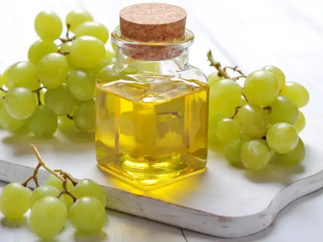 Butelka oleju z pestek winogron, otoczona świeżymi winogronami. Odkryj jego cenne właściwości!