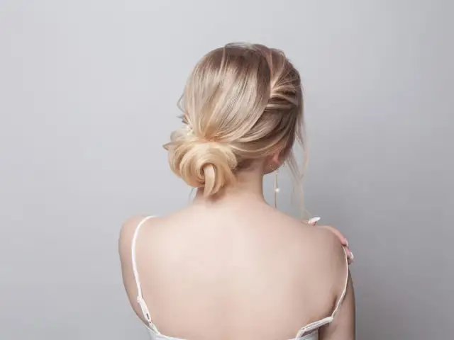 Elegancki kok z blond włosów, spięte spinką z perłą, podkreśla delikatność stylizacji.