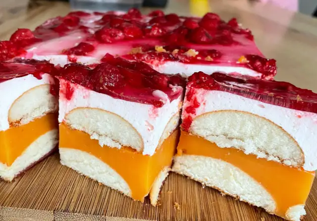Pyszne ciasto z biszkoptami, pomarańczową galaretką i bitą śmietaną, ozdobione malinami.