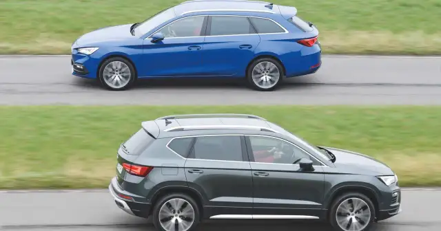 Dwa samochody klasy D: niebieskie kombi i ciemnoszary SUV, jadące obok siebie po drodze.
