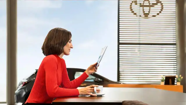 Kobieta w czerwonym swetrze czyta broszurę o gwarancji Toyota Assistance, popijając kawę.