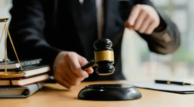 Sędzia trzymający młotek sądowy nad stosem książek i wagą sprawiedliwości.