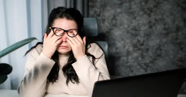 Kobieta w okularach zamyka oczy, masując skronie. Może to być jeden z objawów stwardnienia rozsianego, jak zmęczenie czy bóle głowy.