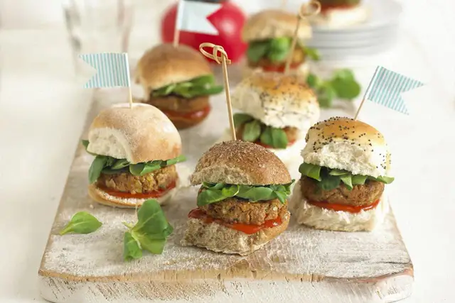 Mini burgery z kotletem, sałatą i flagietkami na desce.