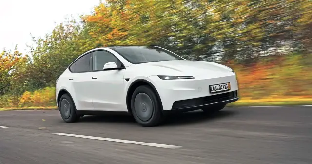 Biały Tesla Y w ruchu, otoczony rozmazanymi jesiennymi drzewami. Czy warto kupić?