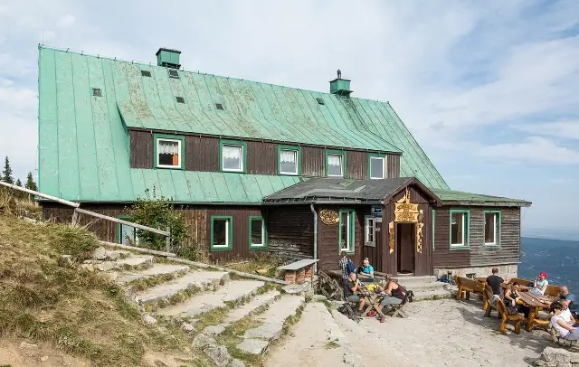 Schronisko pod Łabskim Szczytem, drewniany budynek z zielonym dachem, gdzie turyści odpoczywają przy stolikach.