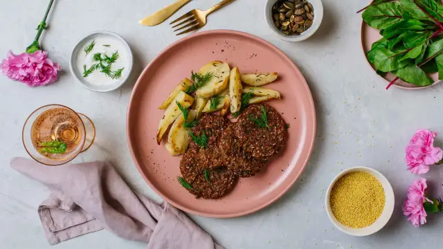 Na talerzu pieczone ziemniaki i kotleciki z kaszy, obok miseczka z jogurtem i koprem. To idealna zdrowa kolacja.