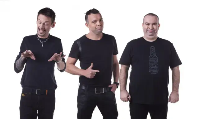 Trzech członków kabaretu Ani Mru Mru w czarnych strojach, każdy z innym wyrazem twarzy i gestem.