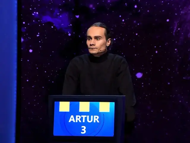 Artur, który wygrał jeden z dziesięciu, stoi na scenie w czarnym golfie.