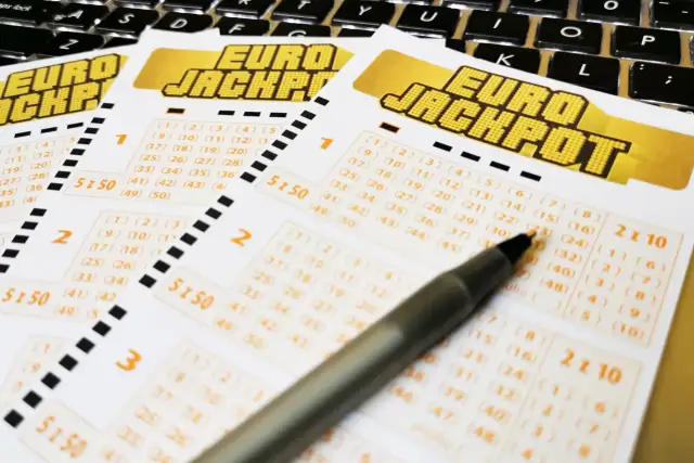 Kupony Eurojackpot leżące na klawiaturze, z długopisem wskazującym na liczby.