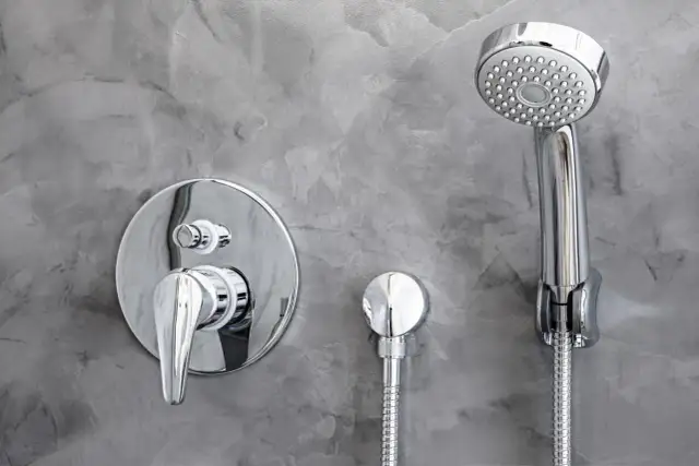 Chromowana deszczownica i bateria podtynkowa na szarej, betonowej ścianie. Dowiedz się, jak zamontować deszczownicę.