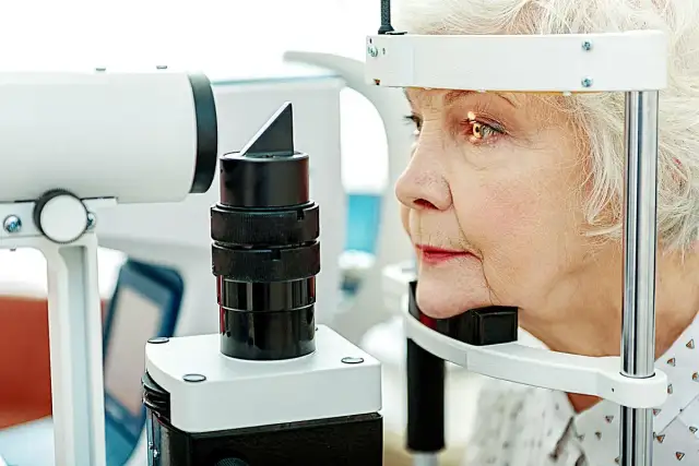 Starsza kobieta podczas badania wzroku przy użyciu sprzętu okulistycznego.
