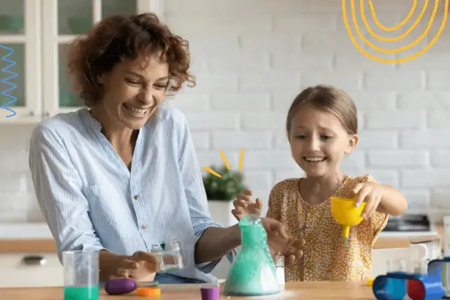 Mama i córka śmieją się, wykonując spektakularne eksperymenty dla dzieci z zieloną pianą w probówce.