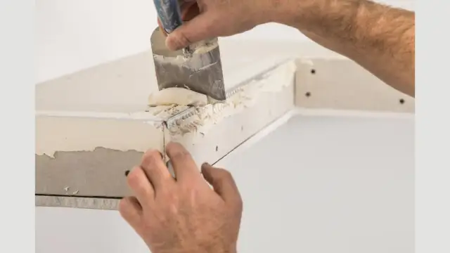 Ręce tynkarza nakładają masę na narożniki do tynkowania, tworząc gładką powierzchnię.