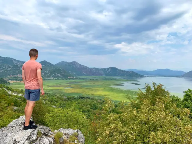 Mężczyzna podziwia rozległe jezioro Szkoderskie z punktu widokowego.