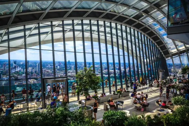 Relaks w Sky Garden w Londynie. Ludzie odpoczywają wśród zieleni, podziwiając panoramę miasta przez szklany dach.