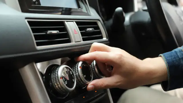 Dłoń kręci pokrętłem klimatyzacji, by włączyć zimne powietrze z nawiewu.