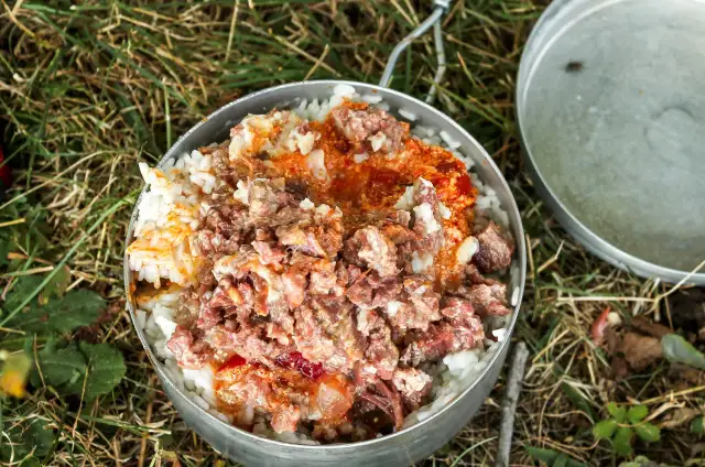 Pyszne jedzenie na biwak: ryż z gulaszem w metalowym garnku, gotowy do spożycia na łonie natury.