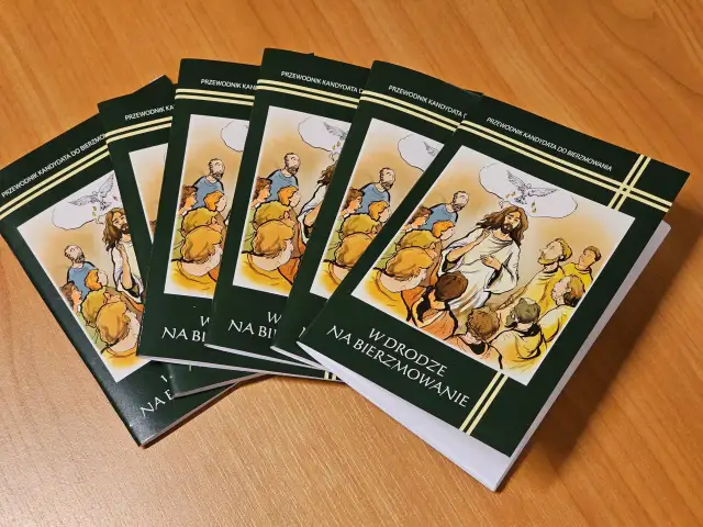 Kilka zielonych książek z ilustracją Jezusa i gołębicy na drewnianym stole.