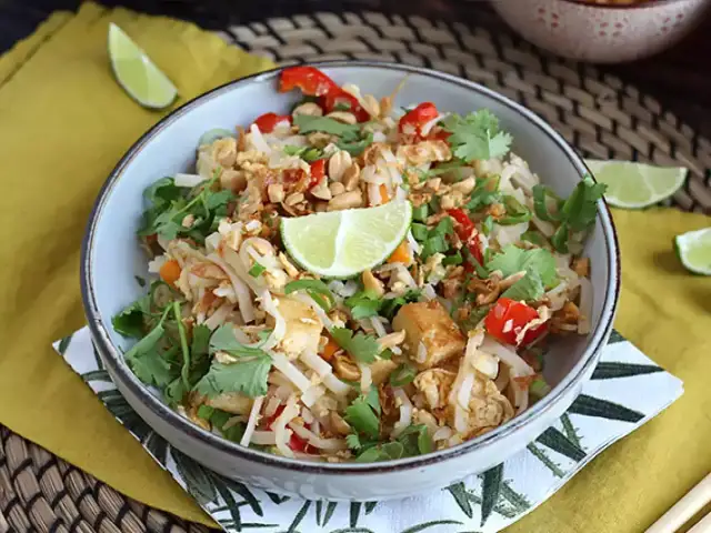 Pyszne pad thai z tofu, posypane orzeszkami ziemnymi i świeżą kolendrą, z kawałkami limonki.