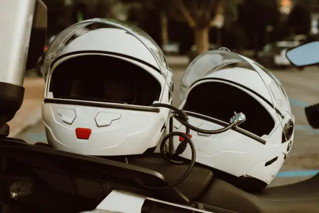Dwa białe kaski motocyklowe połączone linką zabezpieczającą. Mocowanie kasku do motocykla zapewnia bezpieczeństwo podczas postoju.