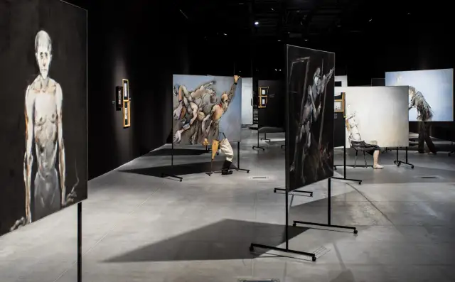 Wystawa malarstwa: ekspozycja prac w ciemnej galerii, z widocznymi postaciami ludzkimi na płótnach.