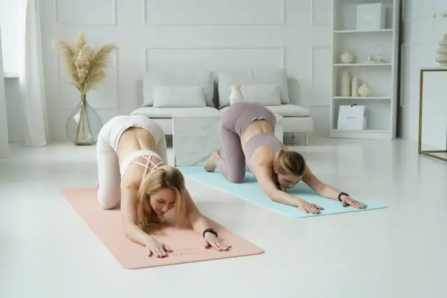 Dwie kobiety ćwiczą jogę w pozycji dziecka na matach w jasnym, minimalistycznym wnętrzu.