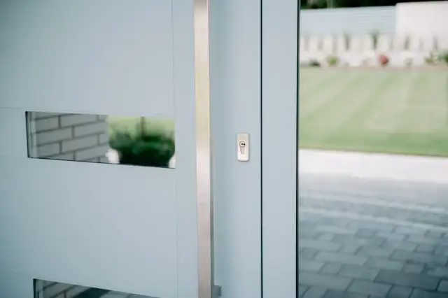 Nowoczesne drzwi wejściowe z metalową klamką i wizjerem. Widoczna regulacja drzwi wejściowych, zapewniająca płynne domykanie.