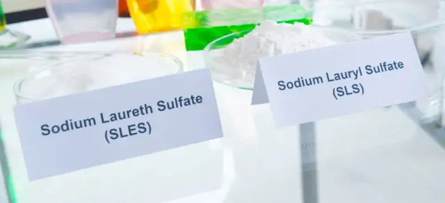 Białe proszki w naczyniach laboratoryjnych, jeden oznaczony jako Sodium Laureth Sulfate (SLES), drugi jako Sodium Lauryl Sulfate (SLS).