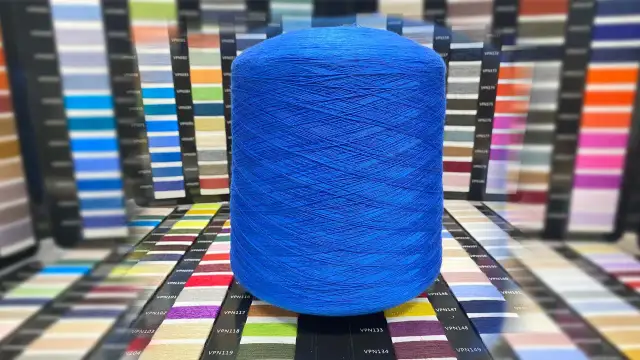 Duża, niebieska rolka włóczki, idealna do tworzenia ubrań z tencelu. W tle palety kolorów.